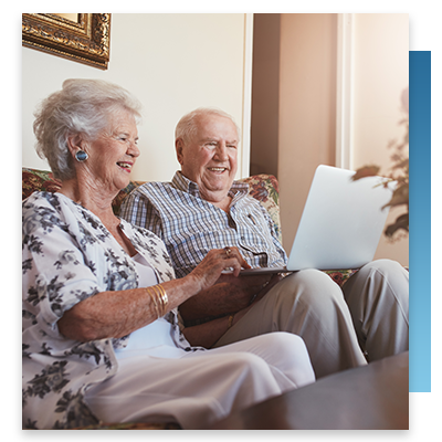 Two elderly people smiling while looking at a laptop
