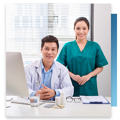 A doctor and nurse smiling while at a desk with a computer on it