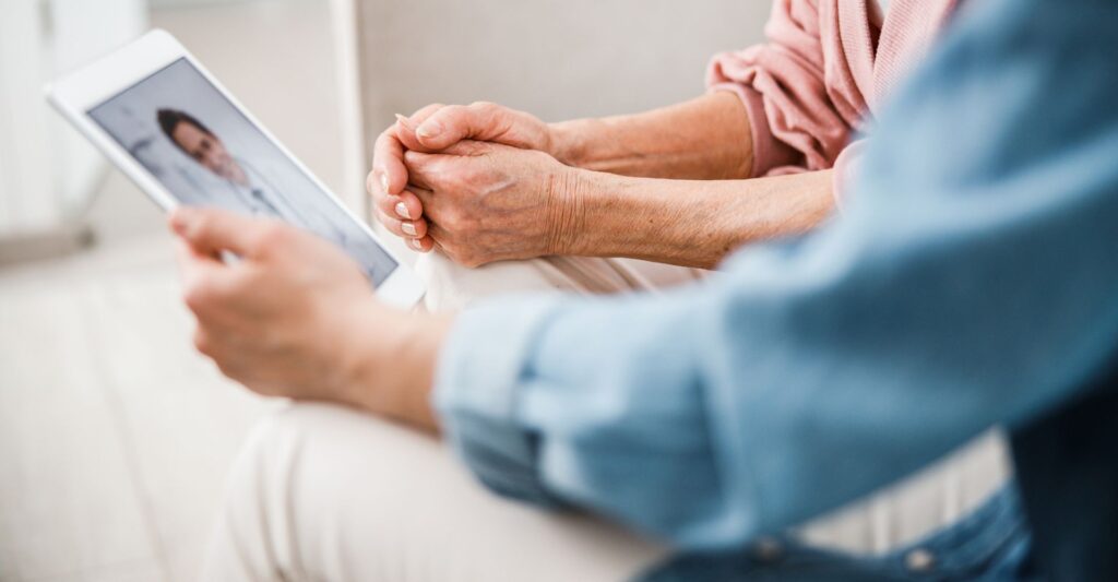 An elderly couples hands holding a tablet while chatting with a doctor