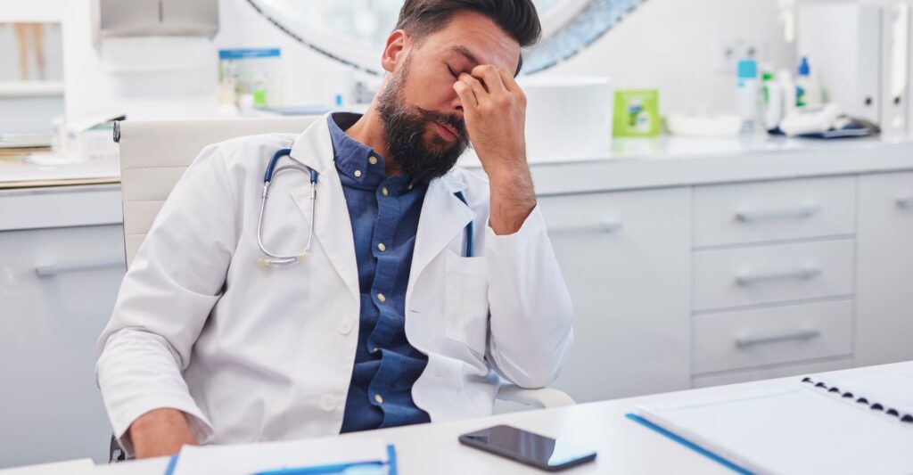 A doctor holding the bridge of his nose because he is tired