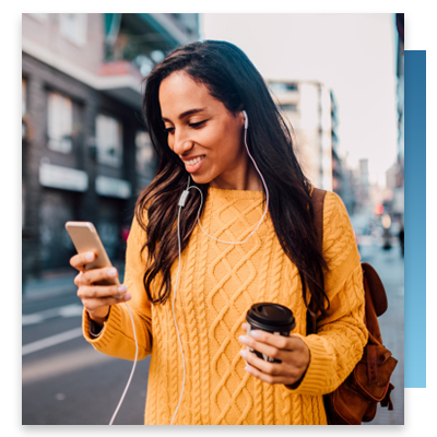 A woman walking around town with a coffee looking at her phone