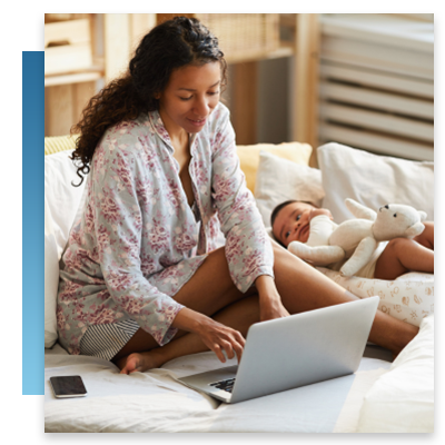 A woman sitting on her bed with her baby using a laptop